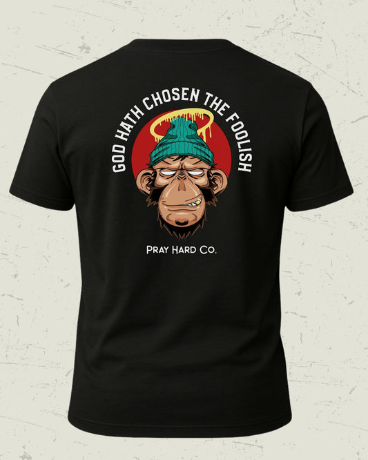 Black t-shirt with a graphic design of a monkey wearing a green beanie and text on a white brick wall background.